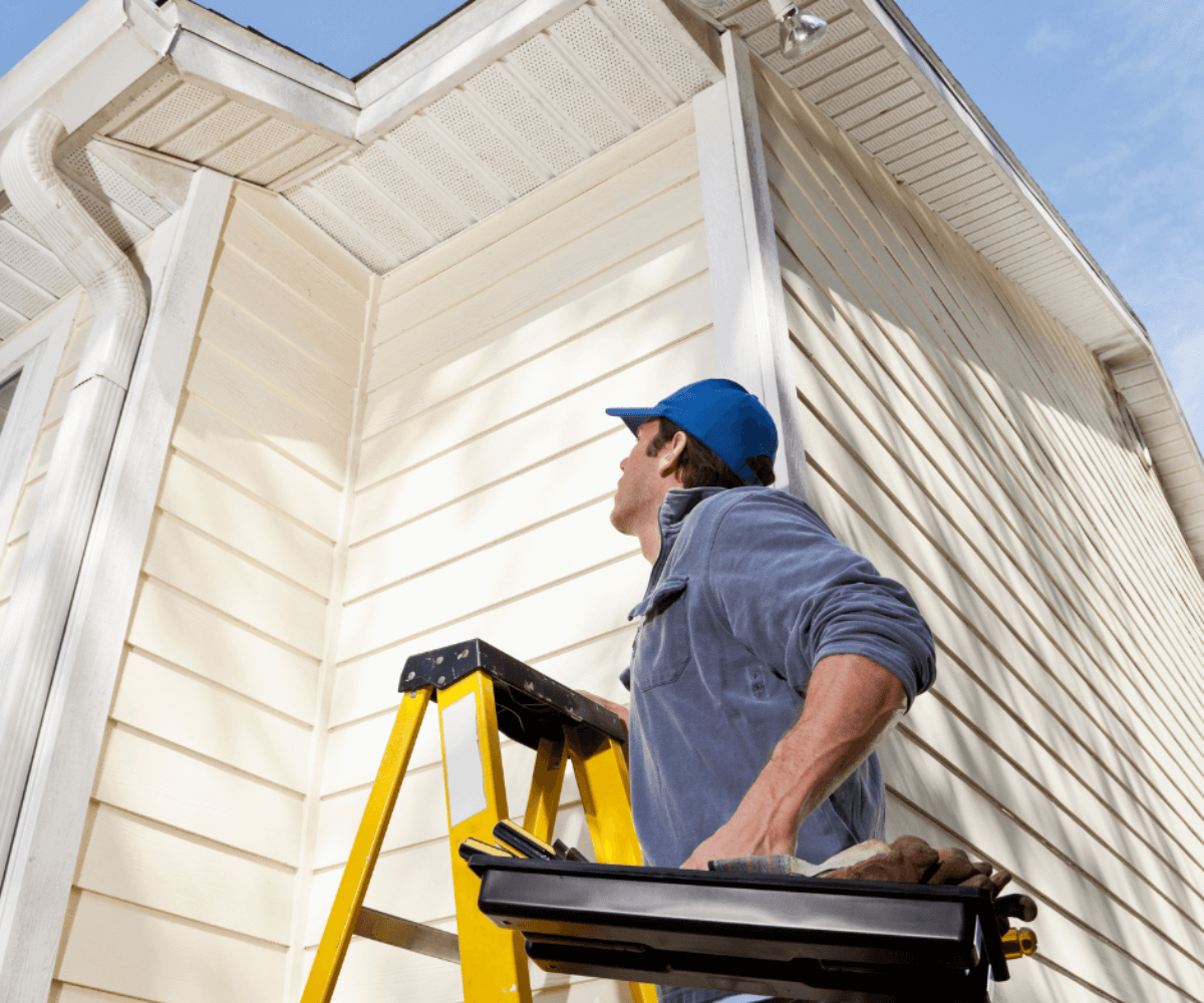 man on yellow ladder repairing house